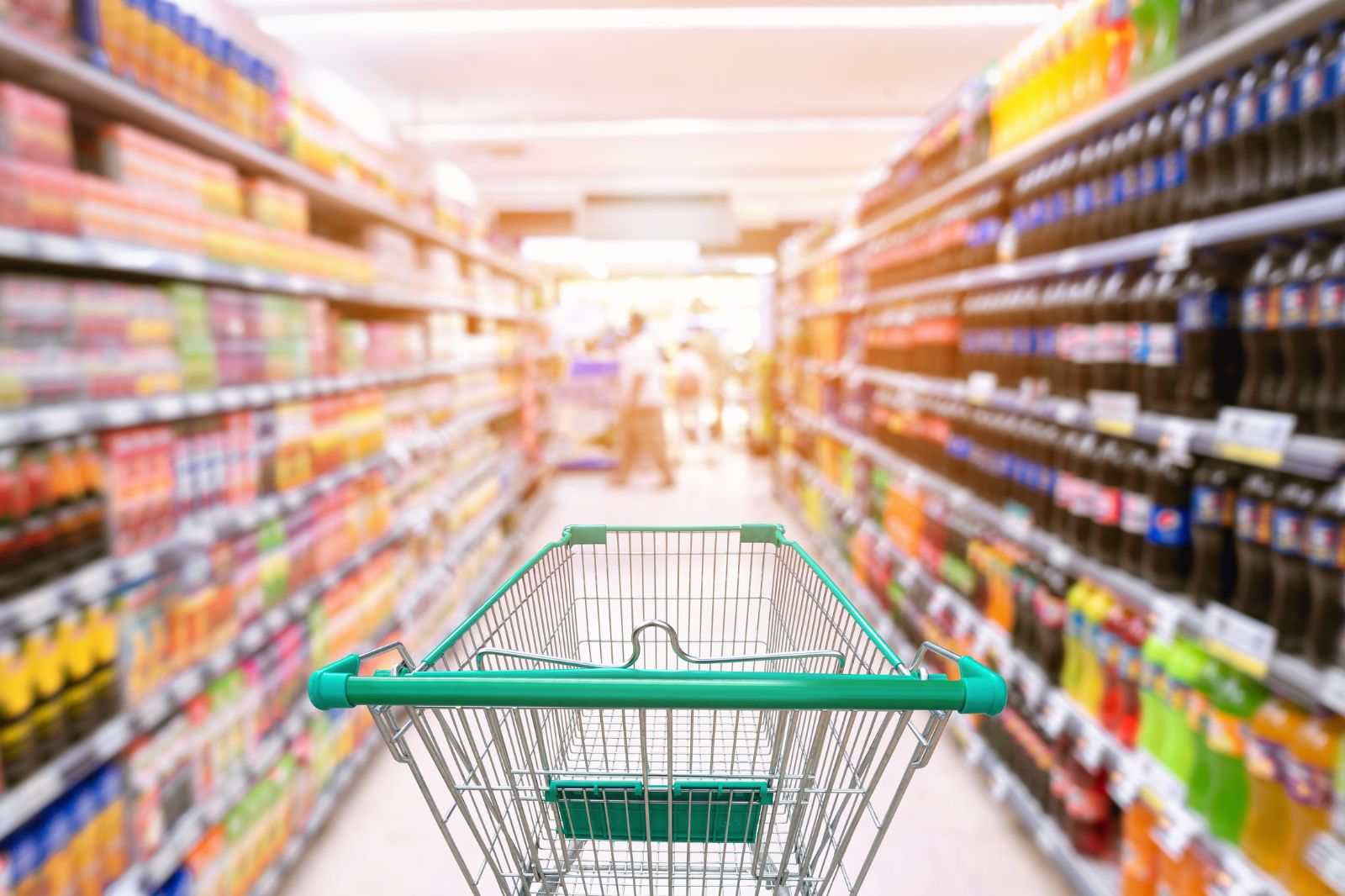 Shopping trolley in grocery store with aisles of ultra-processed foods on either side