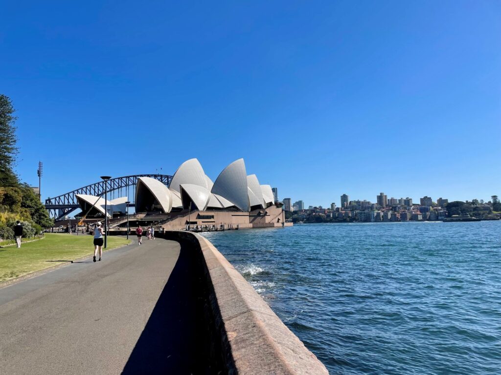 Pathway along the ocean in Sydney with view of Opera House and Sydney Harbour bridge in background