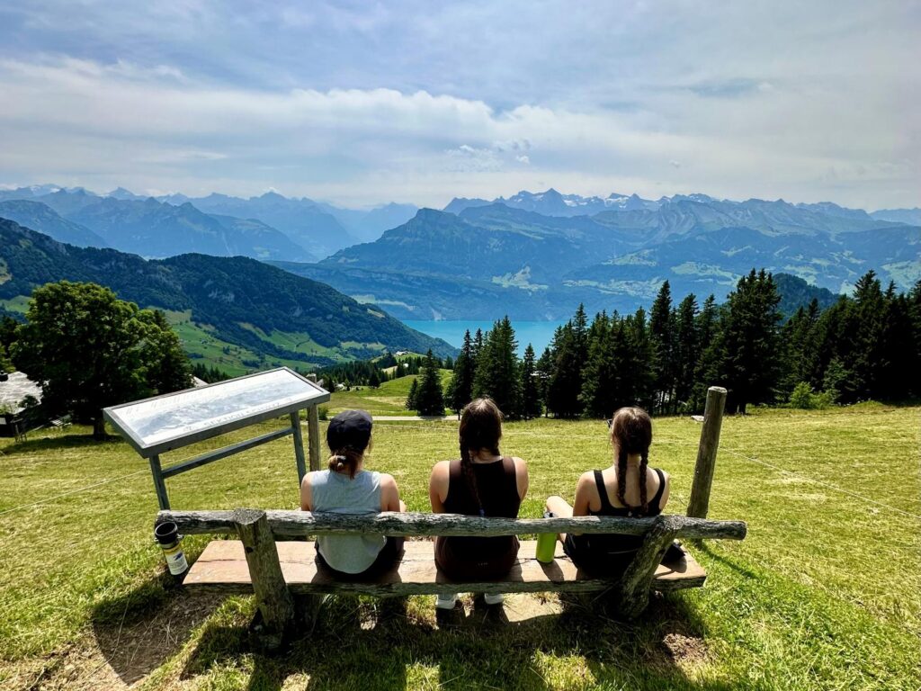 Three girls sit on a bench looking out at the hills in Switzerland with no phones