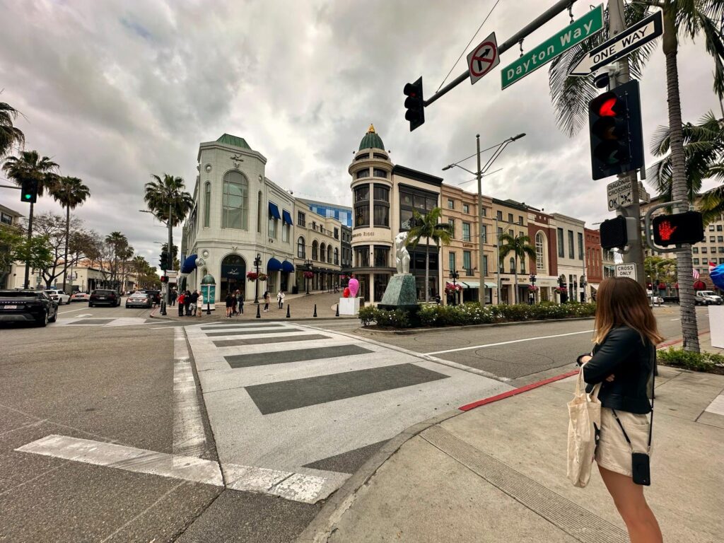 A woman stands on a corner of a street in Beverly Hills taking it in the first time travelling there