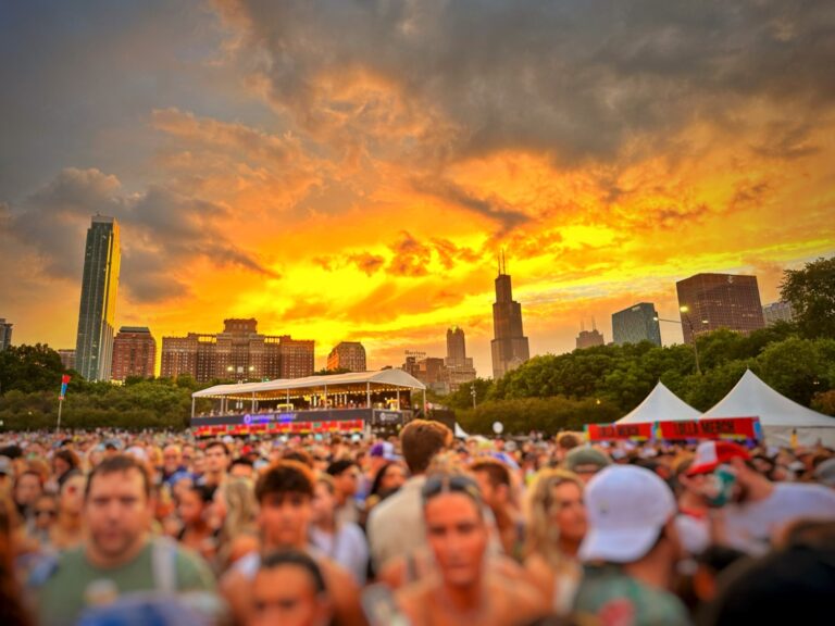 A bright orange sunset over a large crowd at a summer festival