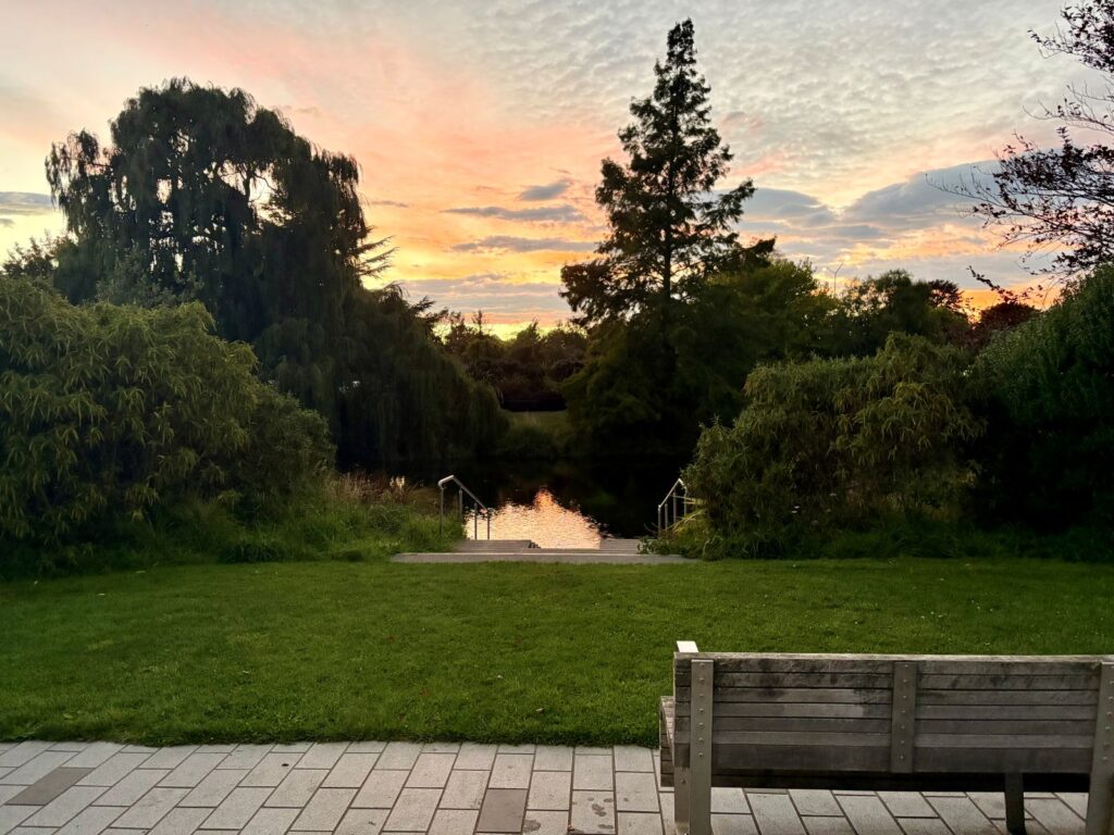 A park bench and river overlooking pink and blue skies at sunrise