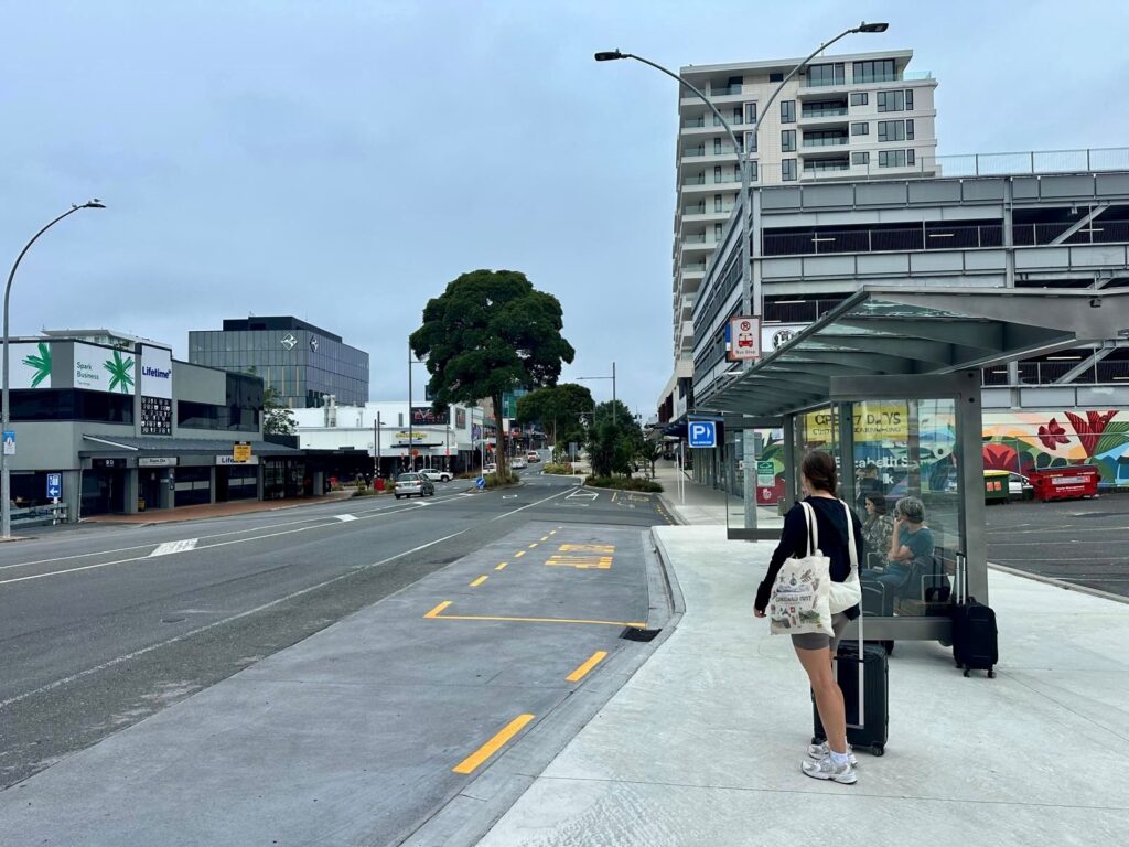 A woman waits at a bus stop in New Zealand, using public transport while travelling