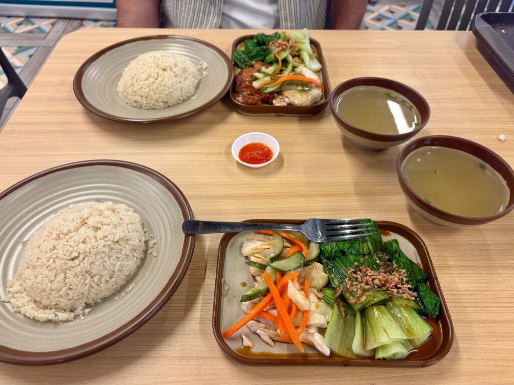 Two plates at a mall food court with Singapore hainanese chicken dish