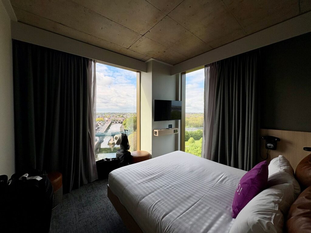 A bed in a hotel room with a city view out the window