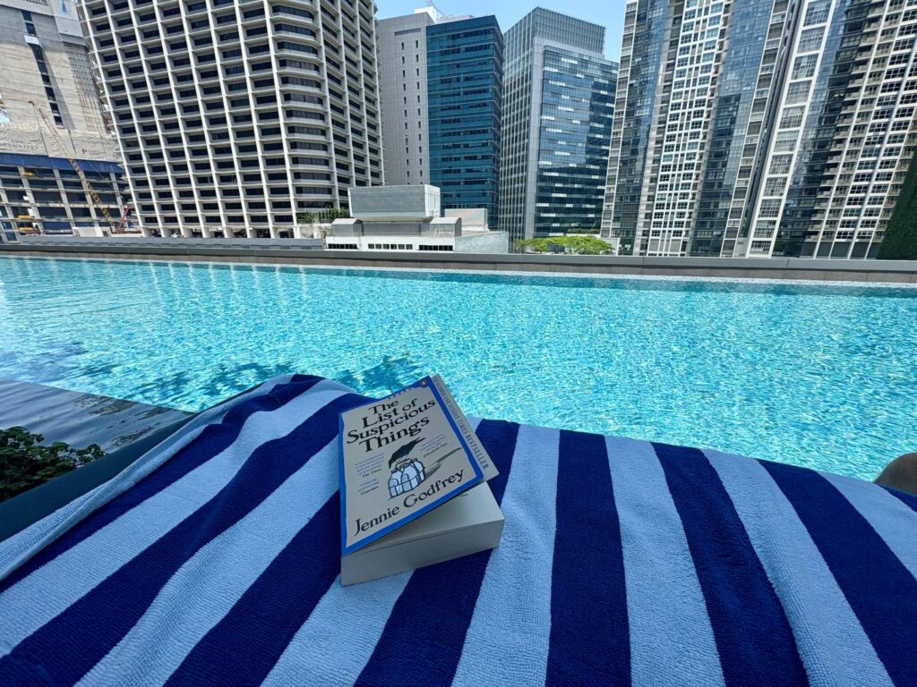 Sitting down looking over a pool with a book in view on a sunny day