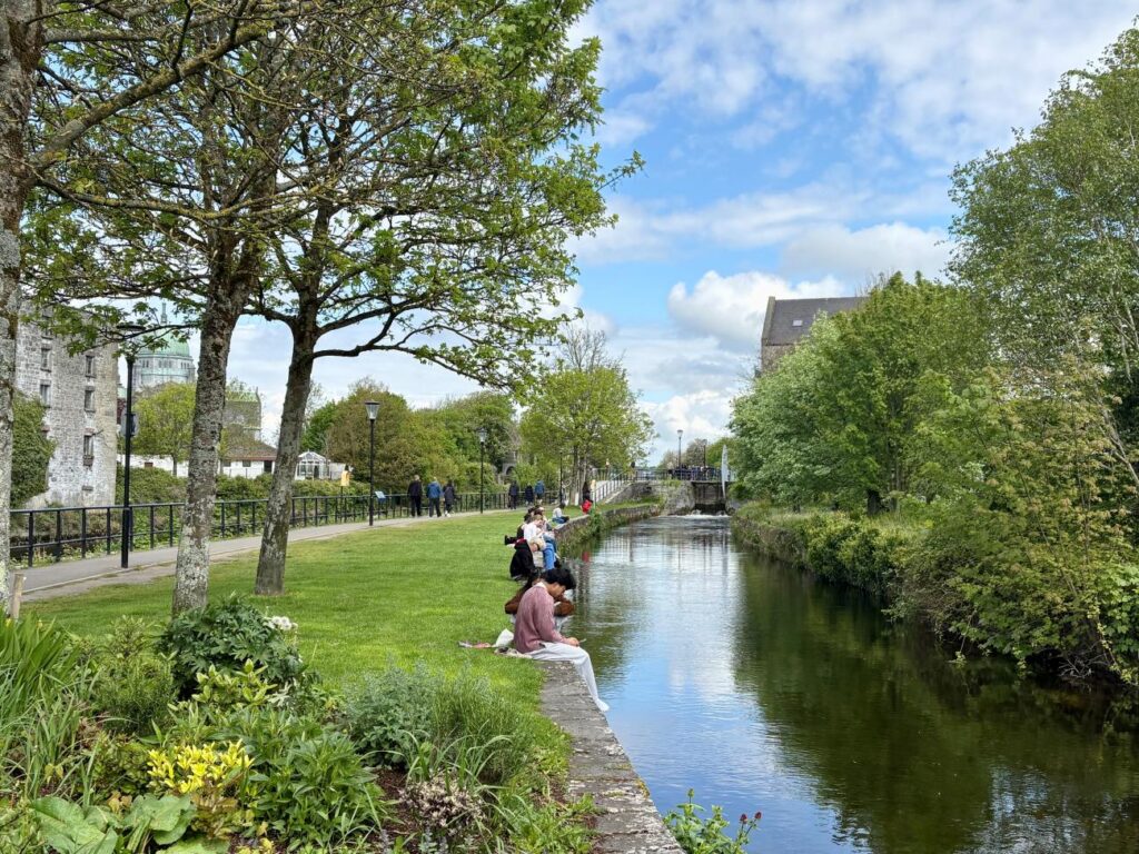 People sitting by a stream in Galway, Ireland on a sunny day
