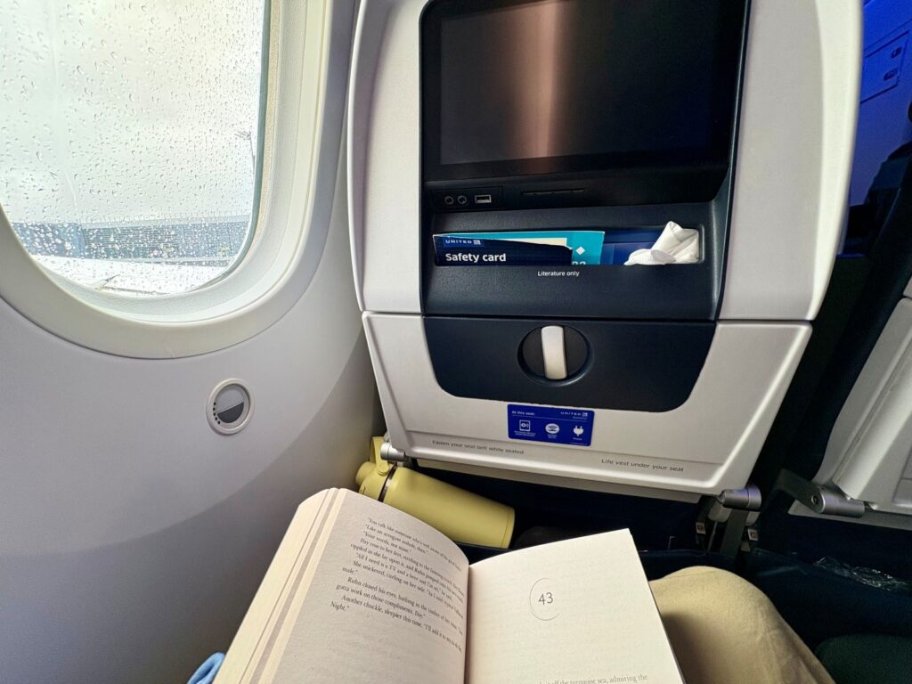 A person reading a book while flying in an aeroplane