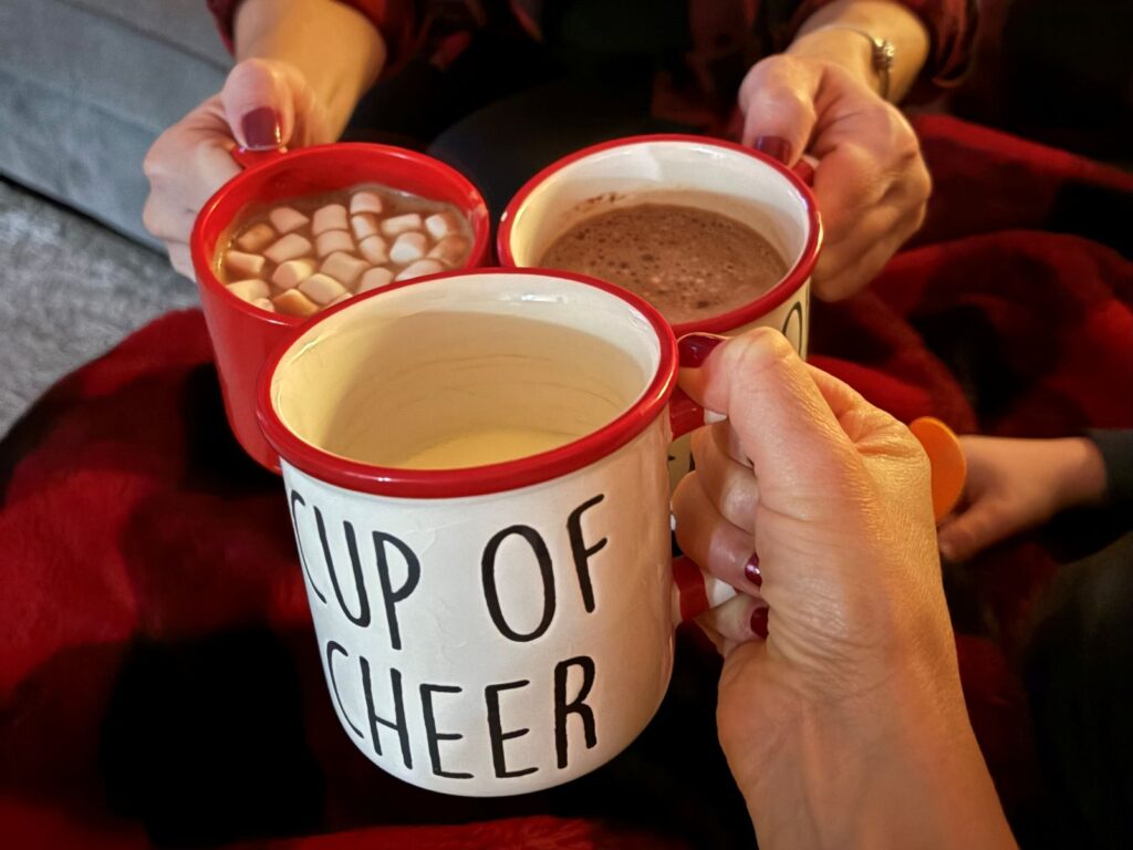 Three people 'cheers' their hot chocolate mugs at Christmas time